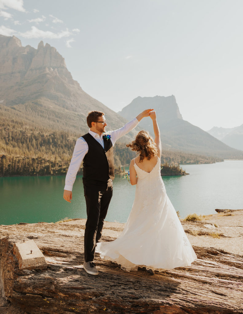 All-Inclusive Elopement Packages in Glacier National Park. Bride and groom dancing after elopement ceremony on cliff in glacier national park.