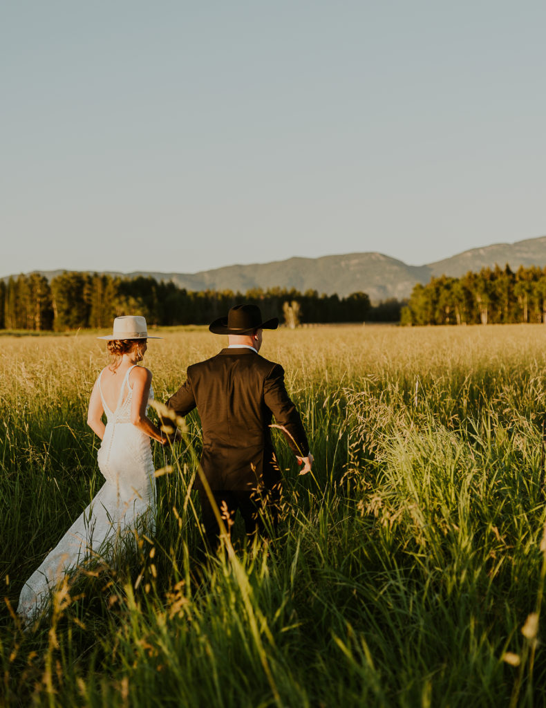 Bride and groom walking in a field. Glacier National Park Photography by Haley Jessat