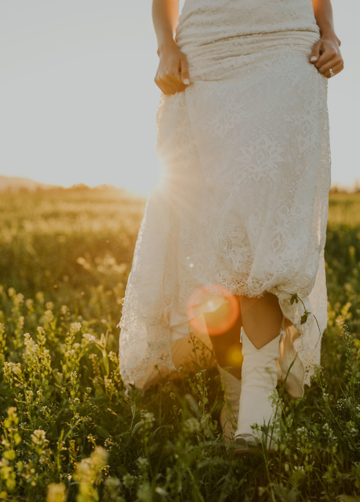 Bride in dress with cowgirl boot in a grassy field. Elopement Photography by Haley Jessat