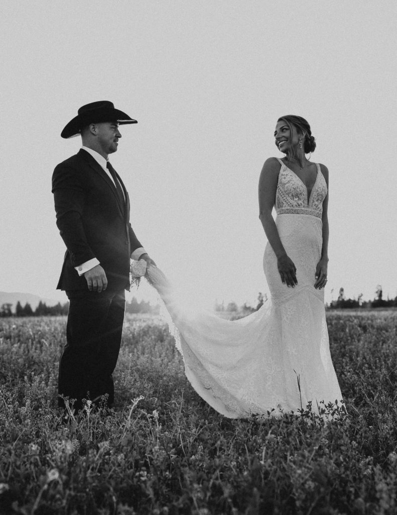Black and white photo of the bride and Groom. Groom is holding the brides dress train. Glacier National Park Photography by Haley Jessat