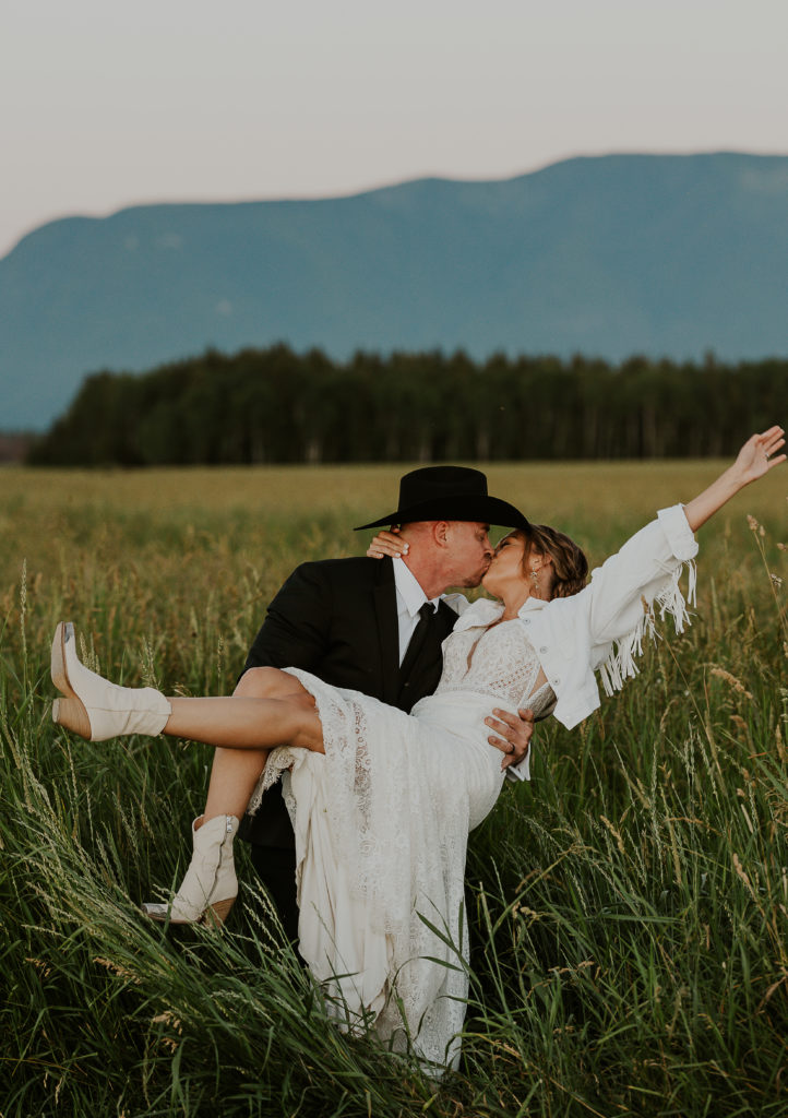 Elopement photography at Glacier Raft Co Wedding and Events in meadow. Groom holding bride in grass field. Photo by Haley Jessat