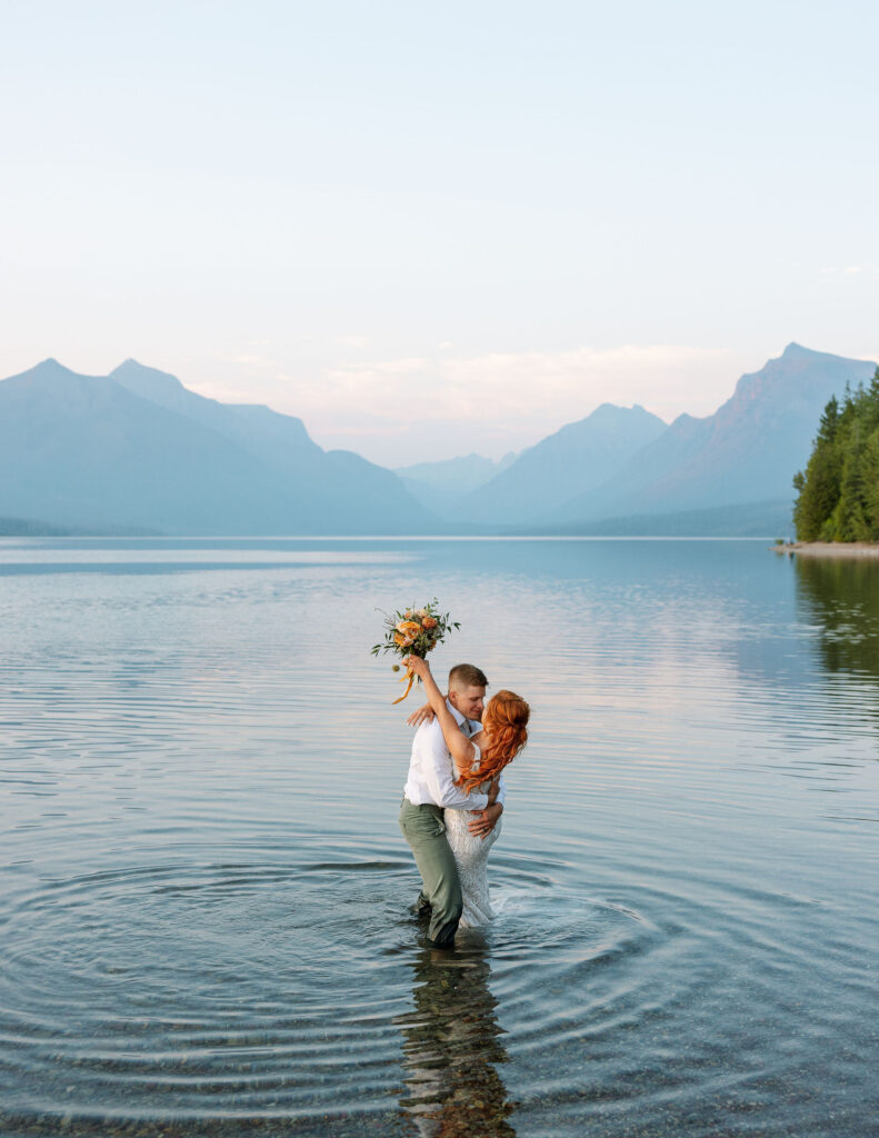 Groom lifting the bride in the water, with mountains in the background, during their Glacier National Park elopement.