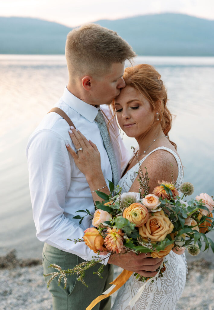 Bride holding a beautiful bouquet, standing close to the groom by the lake during their Glacier National Park elopement.