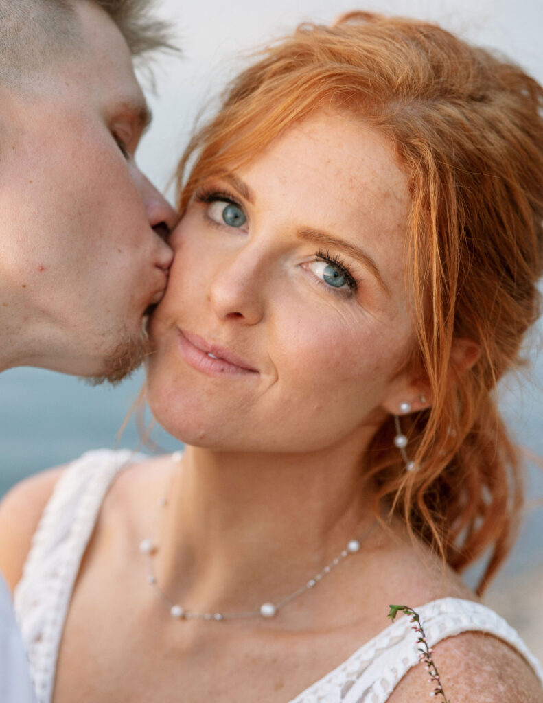 Groom kissing the bride's cheek, with the bride smiling softly during their Glacier National Park elopement.