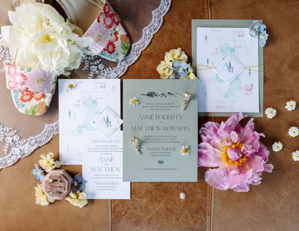 Flat lay of wedding stationery, including invitations and floral details, beautifully arranged with lace and pastel flowers, showcasing the wedding theme at Amen Ranch.