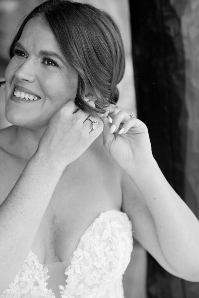 Bride smiling as she puts on her earrings, getting ready for her big day at a Montana ranch wedding venue.