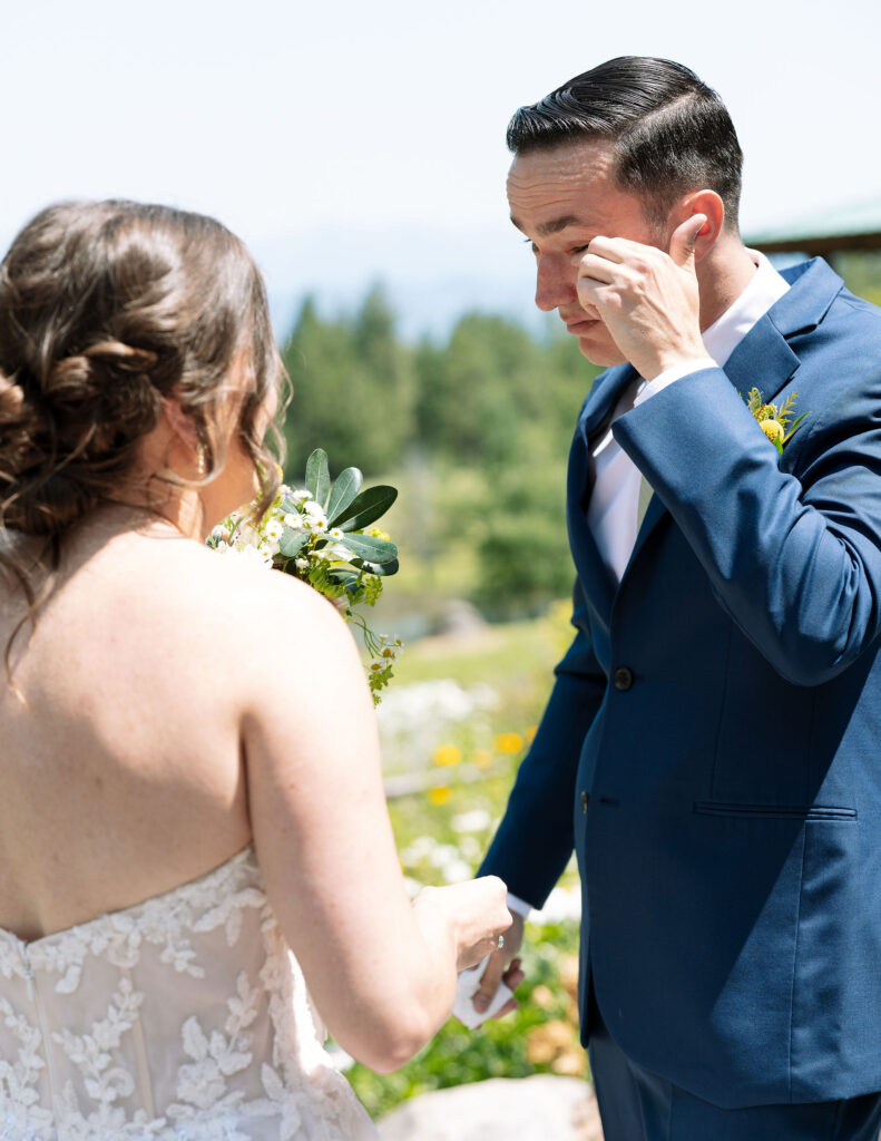 Bride and groom holding hands and exchanging a heartfelt moment, with the groom wiping away a tear during their wedding at a Montana ranch venue.