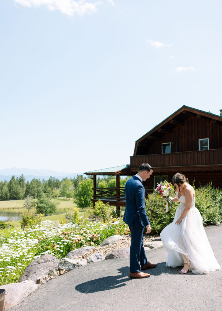 Bride playfully lifting her dress as she walks with the groom, with a rustic Montana ranch cabin in the background, capturing a candid and fun moment at Amen Ranch.