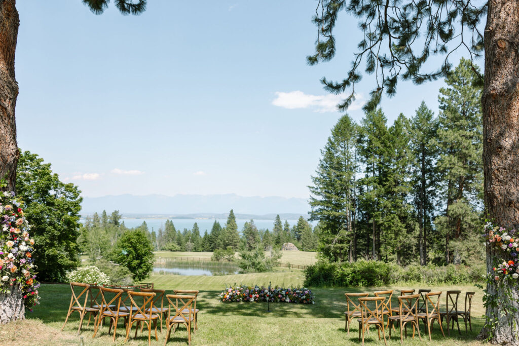 Scenic view of an outdoor wedding ceremony setup with chairs arranged on a grassy lawn, overlooking beautiful mountain views and a serene pond at Amen Ranch.