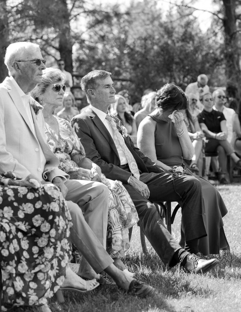 Black and white photo of wedding guests seated during the ceremony, with emotions on their faces, capturing the heartfelt moments at a Montana ranch wedding.