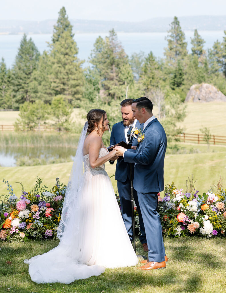 Bride and groom exchanging vows in front of a lush floral arrangement, surrounded by nature and guests, during their wedding ceremony at Amen Ranch.