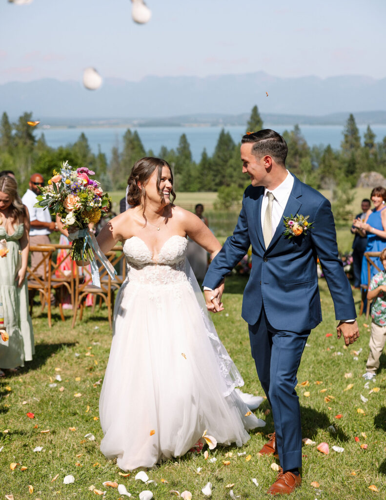 Bride and groom joyfully walking down the aisle, holding hands, with the bride carrying a colorful bouquet, celebrating their wedding ceremony at Amen Ranch.