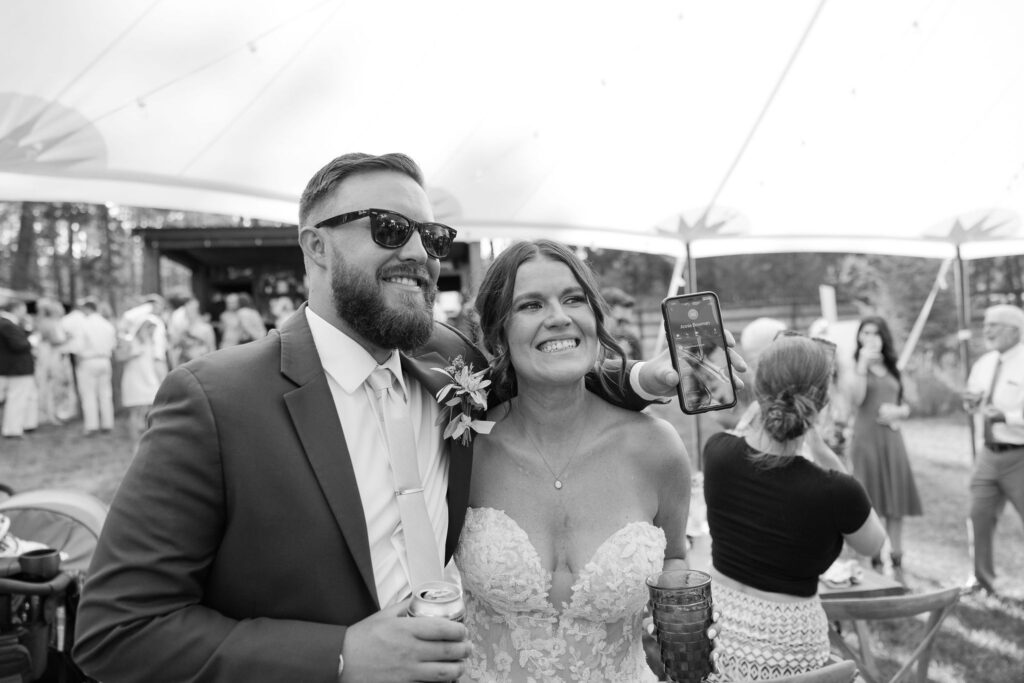 Black and white image of the bride smiling with a guest taking a selfie, capturing a candid and joyful moment during the wedding reception at Amen Ranch.