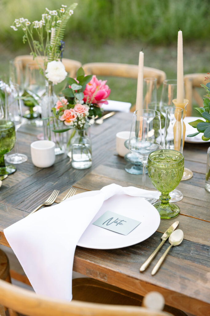 Close-up of a rustic wedding table setting with elegant glassware, green goblets, candles, and fresh floral arrangements, highlighting the decor at a Montana wedding venue.