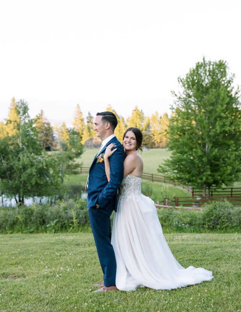 Bride standing behind the groom with a playful smile, enjoying a romantic moment together against a scenic backdrop at Amen Ranch.