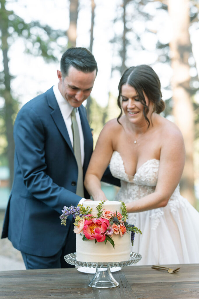 Bride and groom cutting a small, elegantly decorated wedding cake adorned with fresh flowers at their Montana ranch wedding at Amen Ranch.