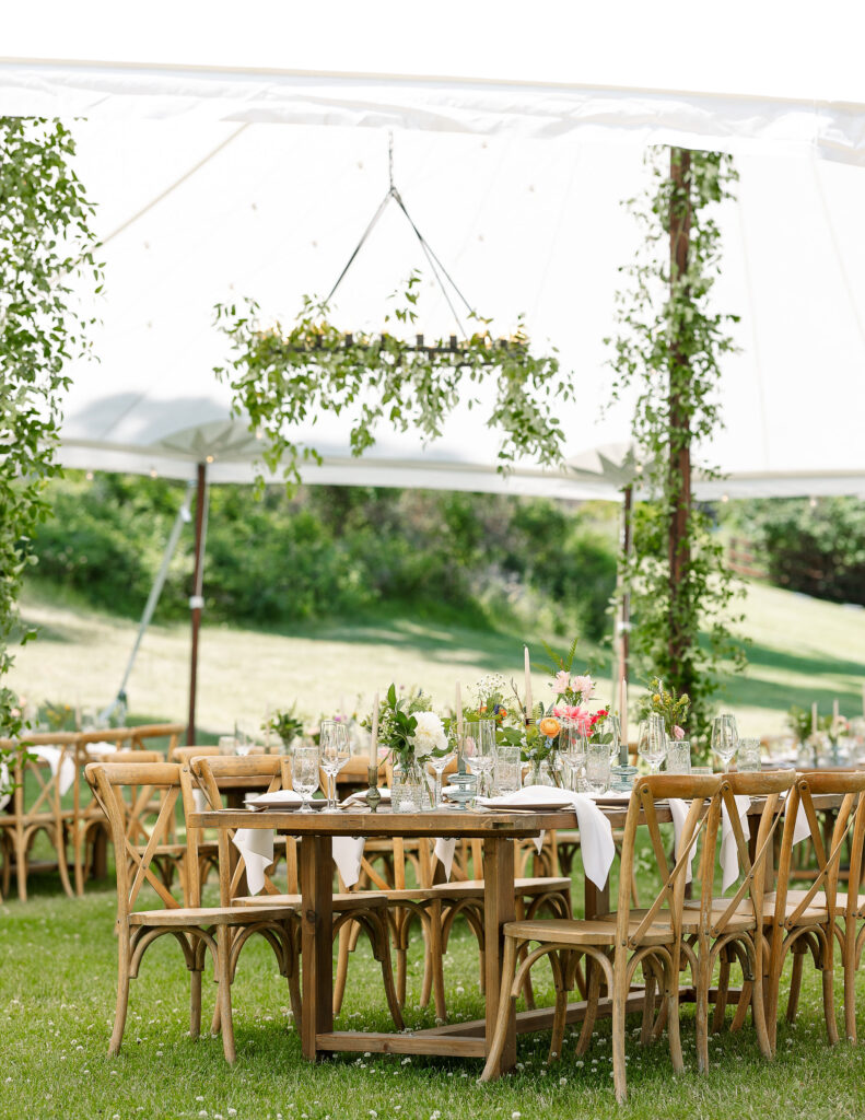 Outdoor reception setup at Amen Ranch wedding venue with rustic wooden chairs and tables under a canopy decorated with greenery, ideal for a Montana ranch wedding.