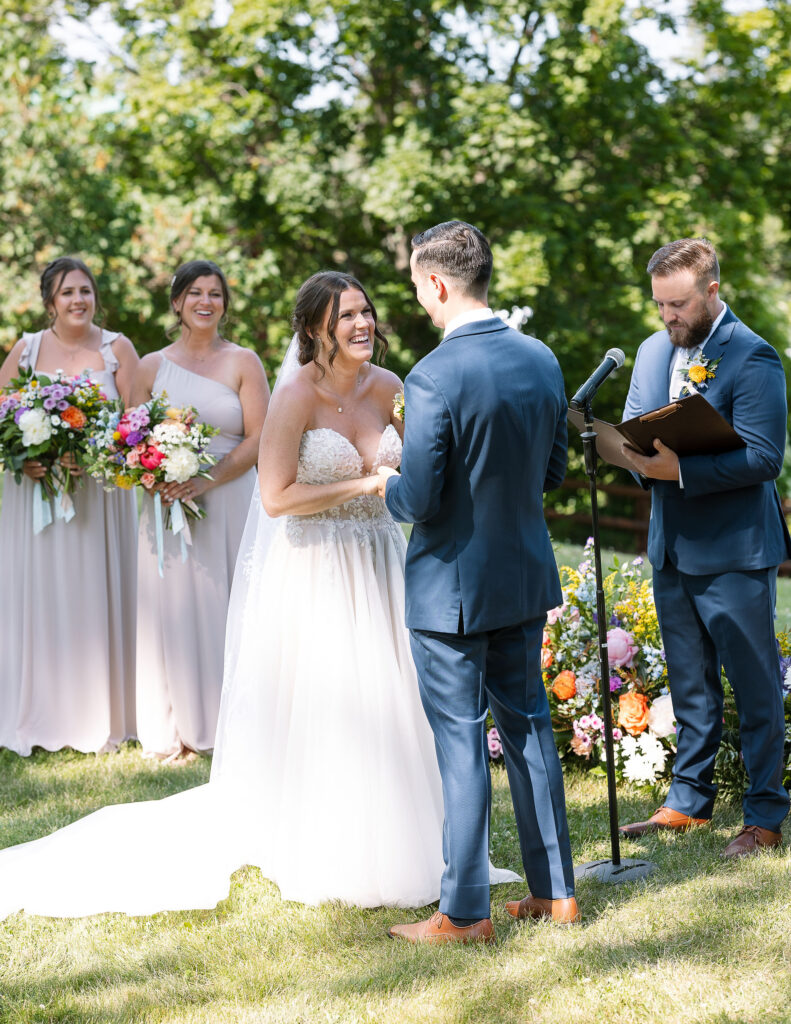 Bride and groom standing face to face during their outdoor ceremony, exchanging vows in front of their wedding party and guests at Amen Ranch.