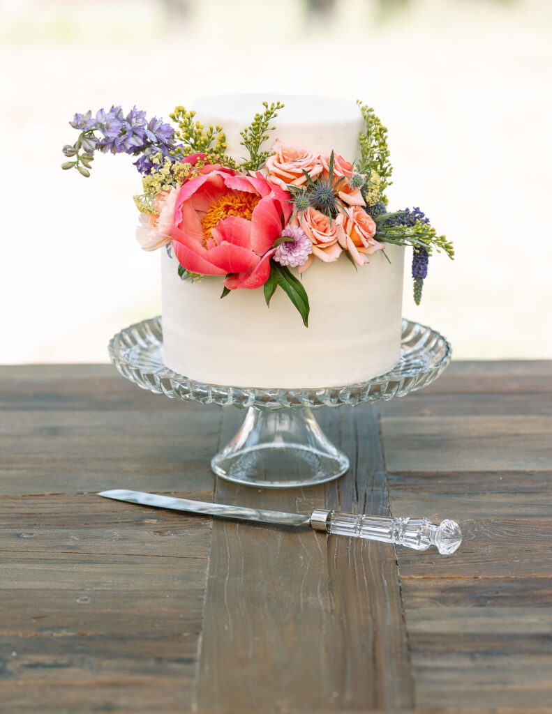 Close-up of a beautifully decorated wedding cake adorned with fresh pink and purple flowers, set on a wooden table at a Montana ranch wedding.