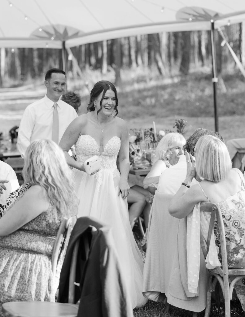 Black and white image of the bride and groom mingling with guests under a tent during the reception, showcasing the joyful celebrations at Amen Ranch in Montana.