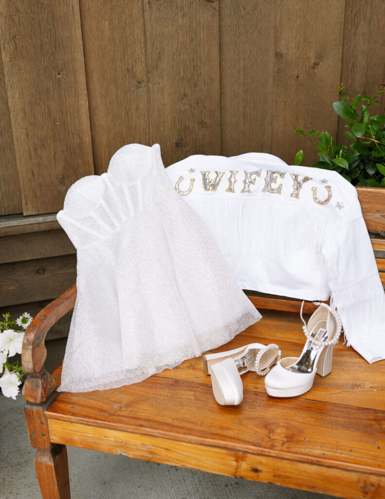 The bride’s "Wifey" jacket and wedding shoes displayed on a rustic bench at Copper Rose Ranch Wedding Venue. Captured by Montana Wedding Photographer Haley J Photo.

