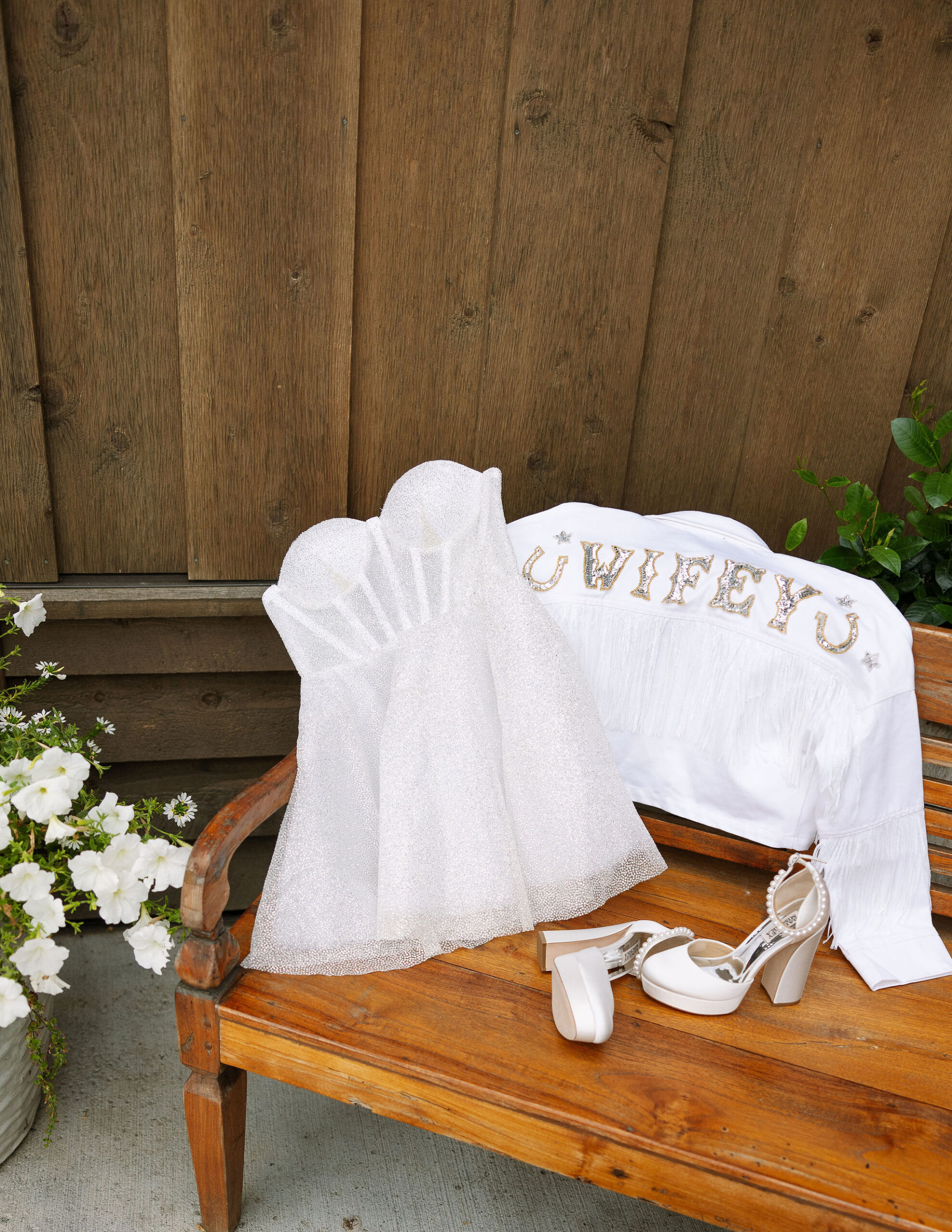 A close-up of the bride’s "Wifey" jacket and sparkly wedding shoes placed on a rustic bench at Copper Rose Ranch Wedding Venue. Captured by Montana Wedding Venue Photographer Haley J Photo.