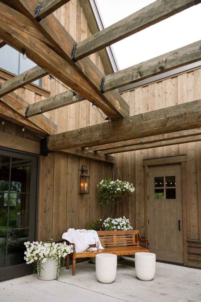 A cozy seating area with wooden benches and potted plants outside the rustic entrance of Copper Rose Ranch Wedding Venue. Captured by Haley J Photo, a Montana Wedding Venue Photographer.