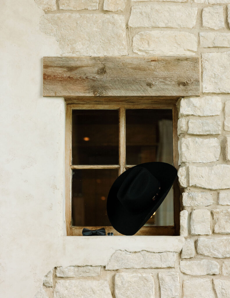 A black cowboy hat placed on a rustic window ledge against a stone wall at Copper Rose Ranch Wedding Venue. Captured by Montana Wedding Photographer Haley J Photo.