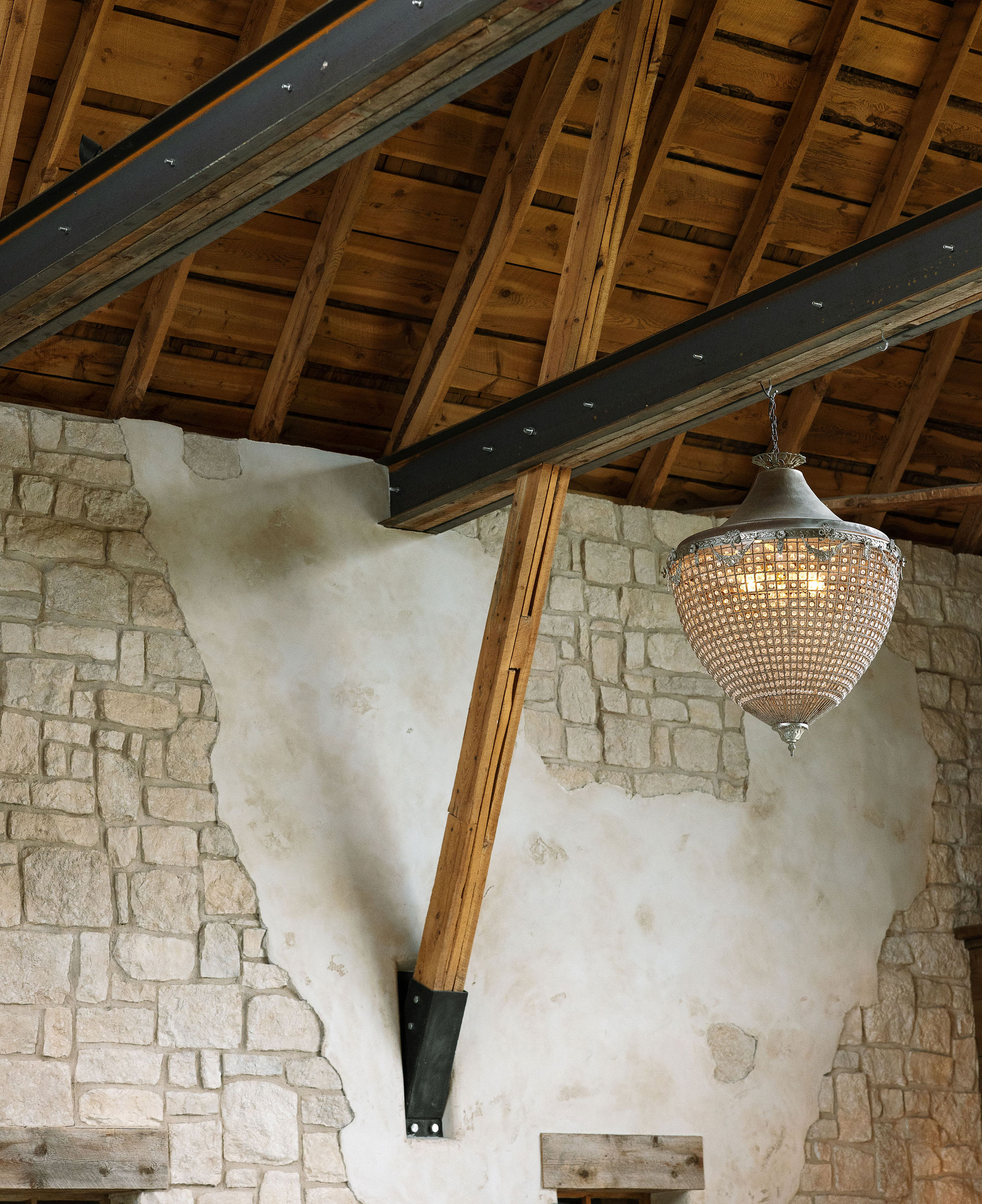 A close-up of the rustic wooden beams and chandelier inside the barn at Copper Rose Ranch Wedding Venue in Montana. The architectural details are highlighted in this shot by Haley J Photo, a Montana Wedding Photographer.