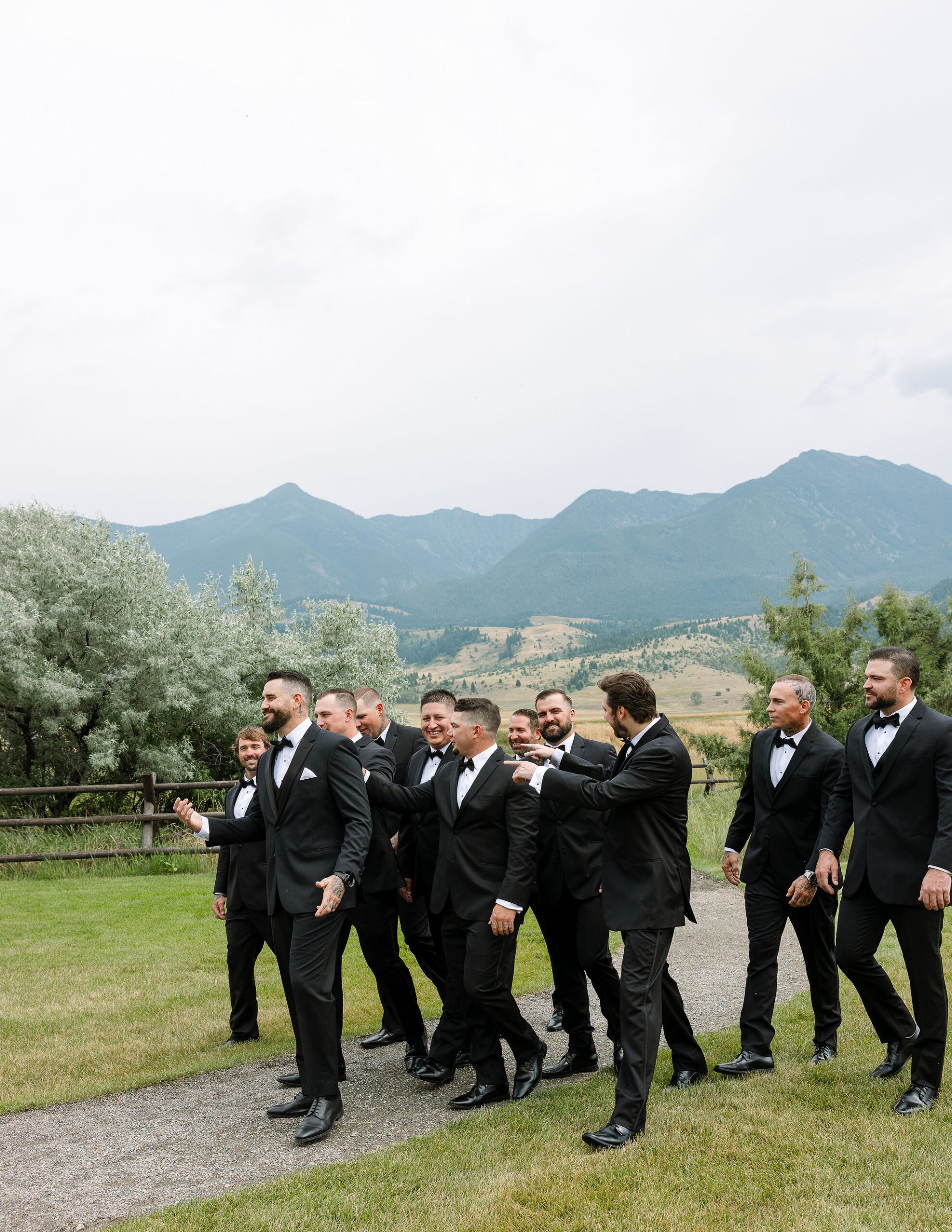 The groom and his groomsmen walk towards the ceremony location at Copper Rose Ranch Wedding Venue, with the Montana mountains as a dramatic backdrop. The group is elegantly dressed in black suits, captured by Montana Wedding Photographer Haley J Photo.