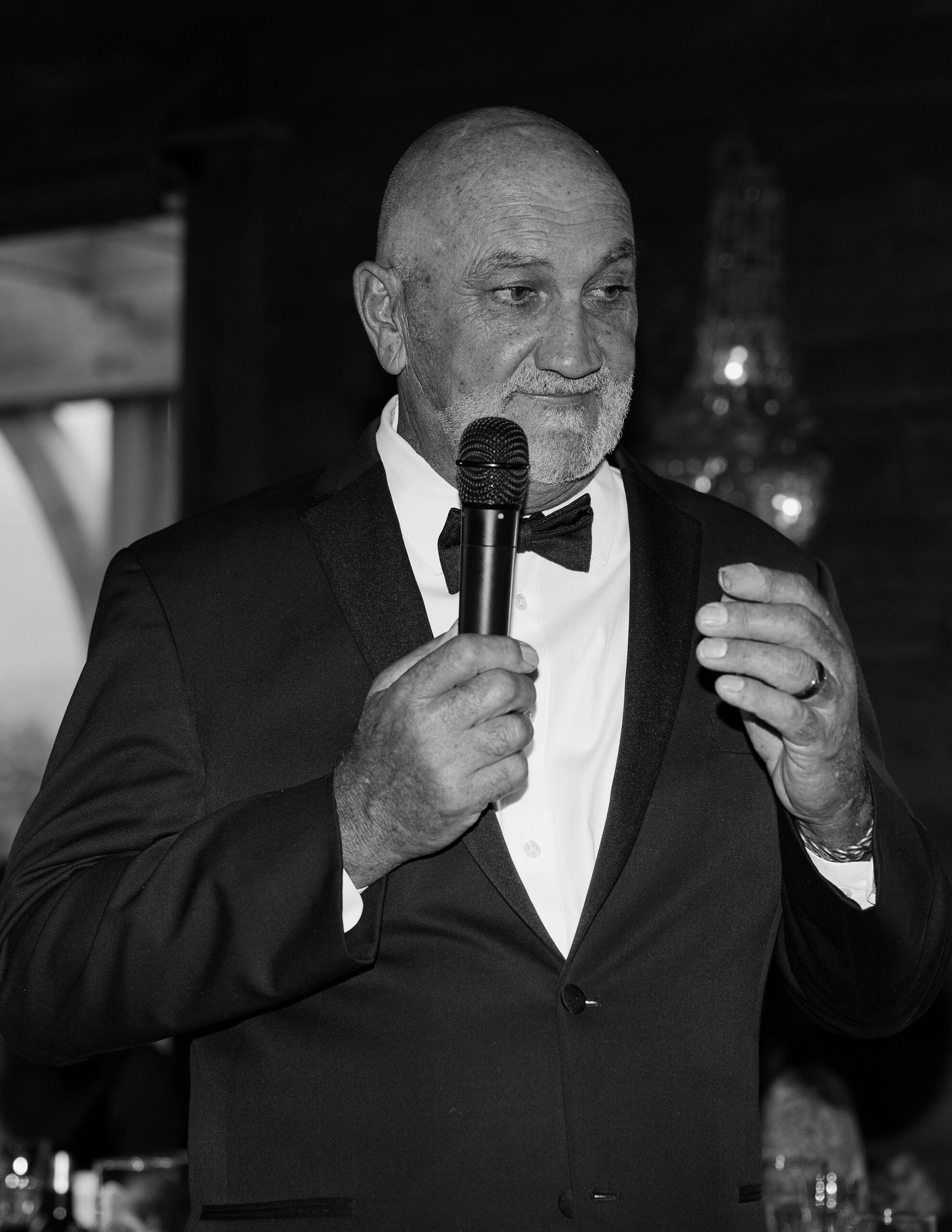 A close-up, black and white image of an older man giving a heartfelt speech during the reception at Copper Rose Ranch Wedding Venue. His expression conveys emotion, beautifully captured by Haley J Photo, a Montana Wedding Venue Photographer.