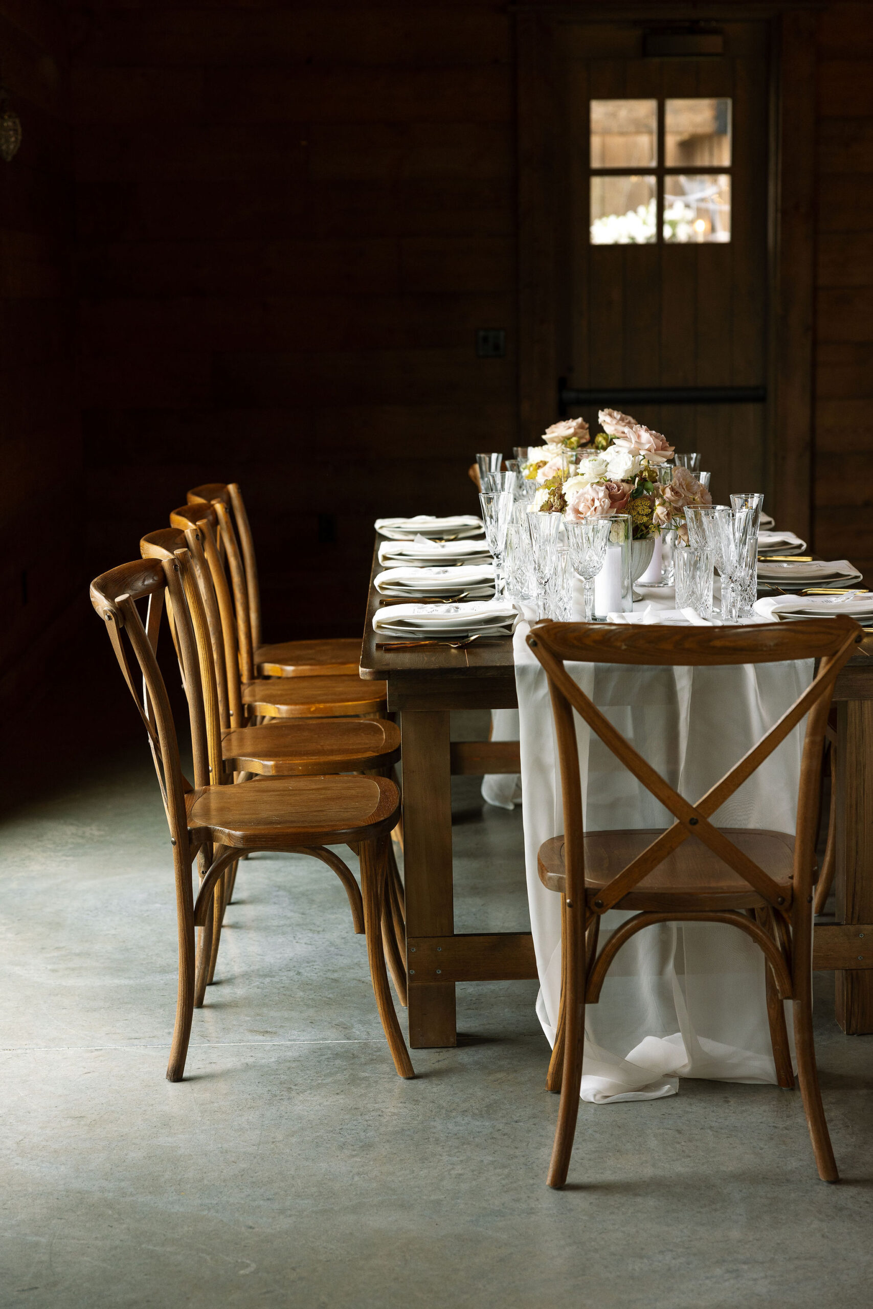 An intimate table setting for a smaller group at Copper Rose Ranch Wedding Venue in Montana. The wooden table and chairs, along with soft floral centerpieces, create a cozy and elegant atmosphere, captured by Haley J Photo, a Montana Wedding Venue Photographer.