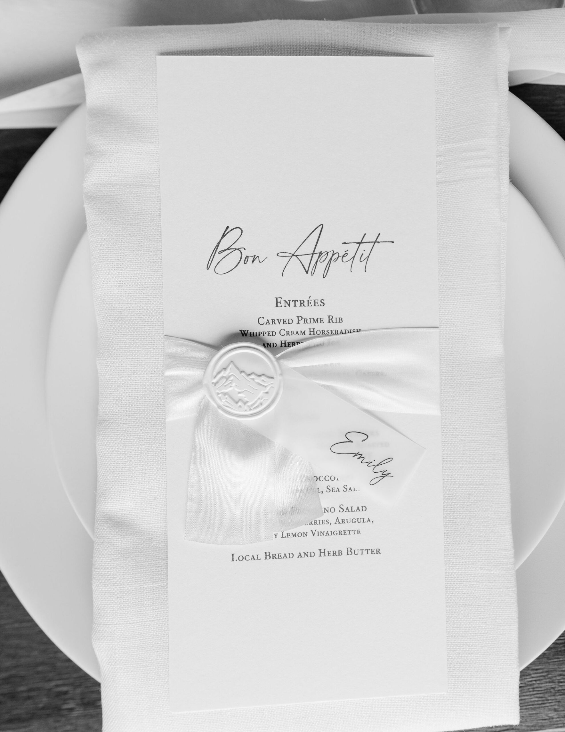 A place setting at Copper Rose Ranch Wedding Venue, featuring a white linen napkin with an elegantly printed menu and a wax seal. The sophisticated details of the Montana Bride's wedding are highlighted by Montana Wedding Photographer Haley J Photo.