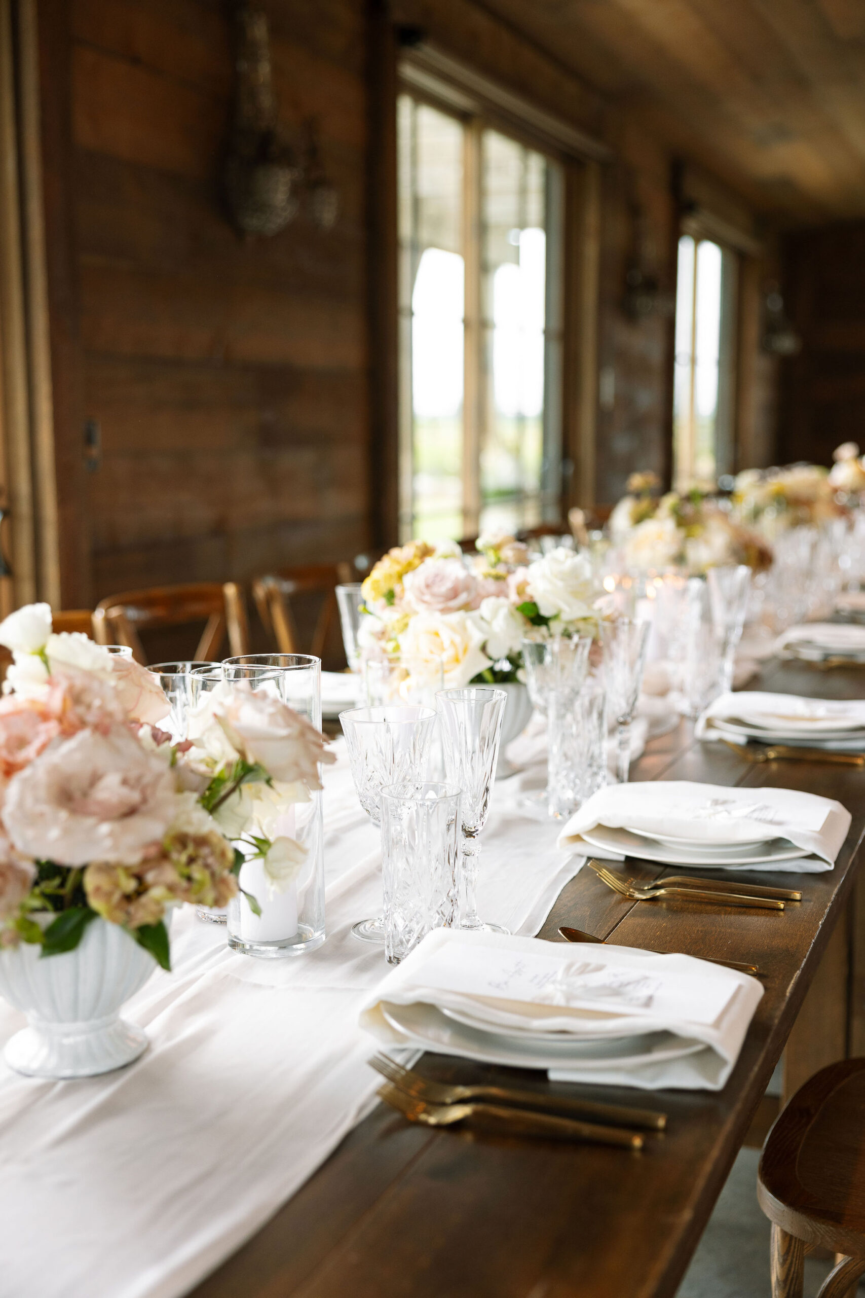 A close-up of the meticulously set dining table at Copper Rose Ranch Wedding Venue, featuring crystal glassware, gold utensils, and soft pink and white floral centerpieces. The attention to detail is beautifully captured by Haley J Photo, a Montana Wedding Venue Photographer.