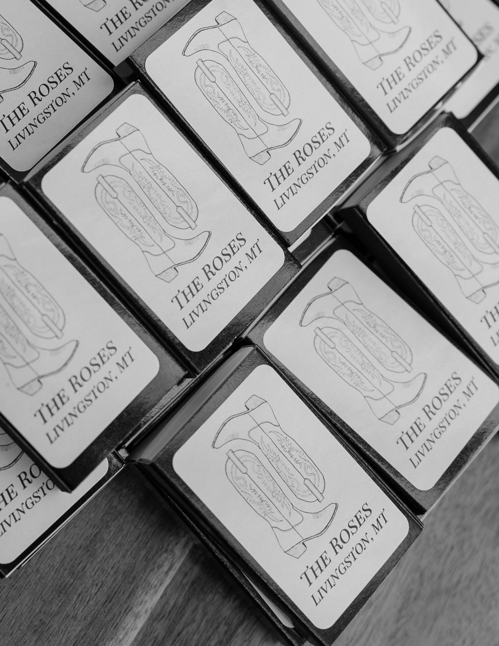  Custom matchboxes with a design featuring the Copper Rose Ranch logo, set out as wedding favors for guests. The black and white image emphasizes the personalized details, captured by Montana Wedding Photographer Haley J Photo.