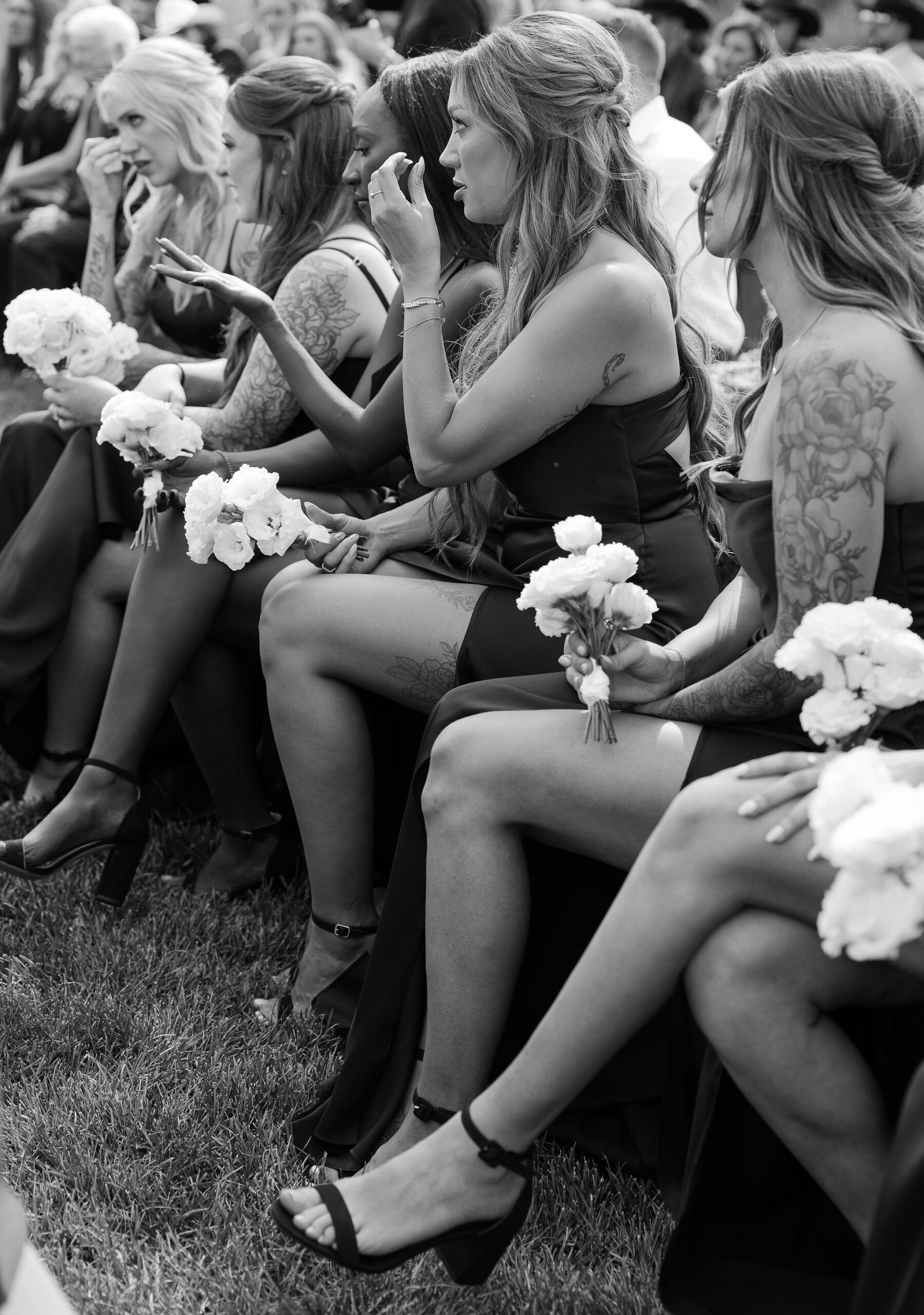  A black and white photo of bridesmaids sitting during the ceremony at Copper Rose Ranch Wedding Venue, holding white bouquets. The emotion on their faces is clearly visible, and the moment is sensitively captured by Montana Wedding Photographer Haley J Photo.