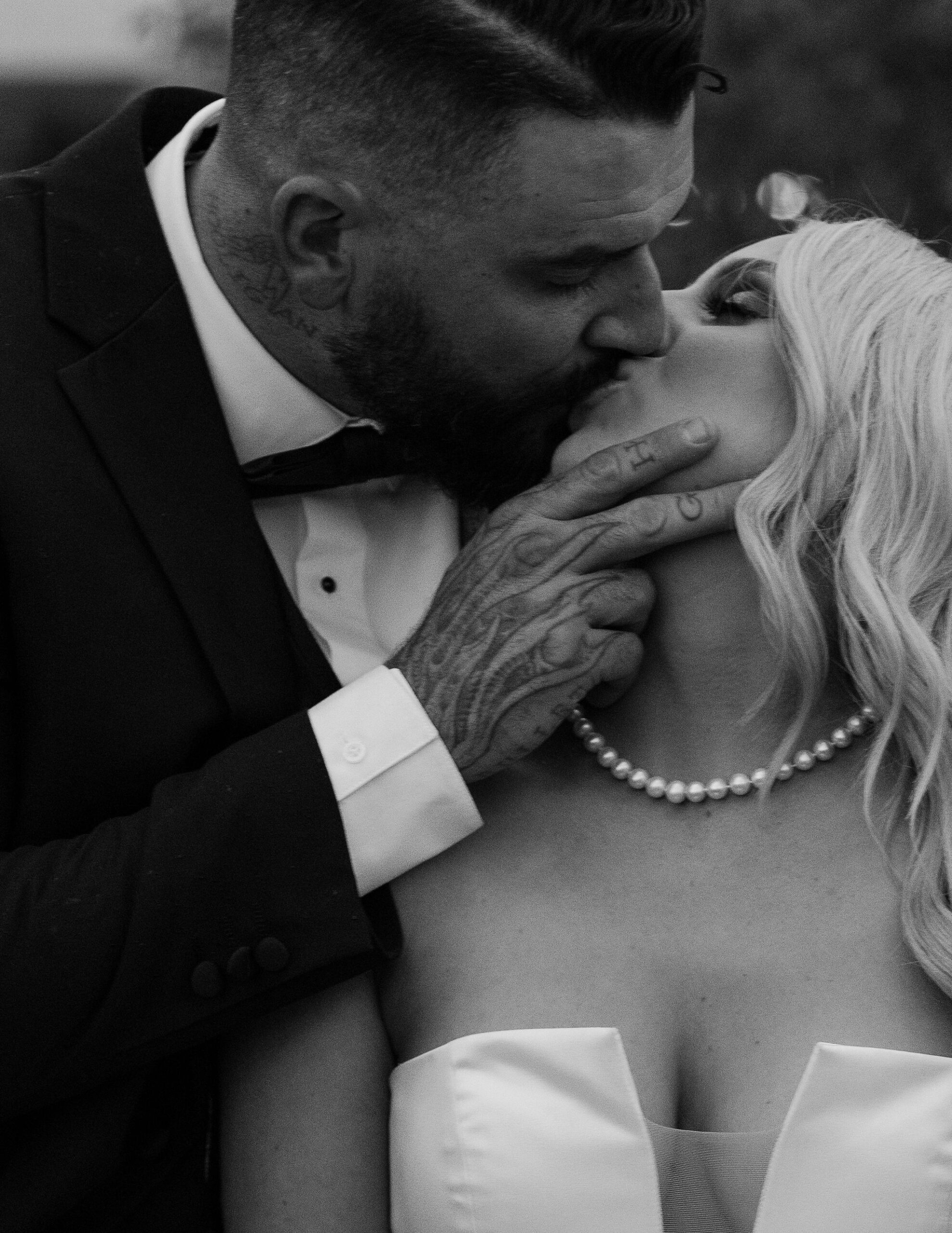 A close-up, black and white image of the groom tenderly kissing the bride as they embrace at Copper Rose Ranch Wedding Venue. The intimate and emotional moment is captured by Montana Wedding Photographer Haley J Photo.