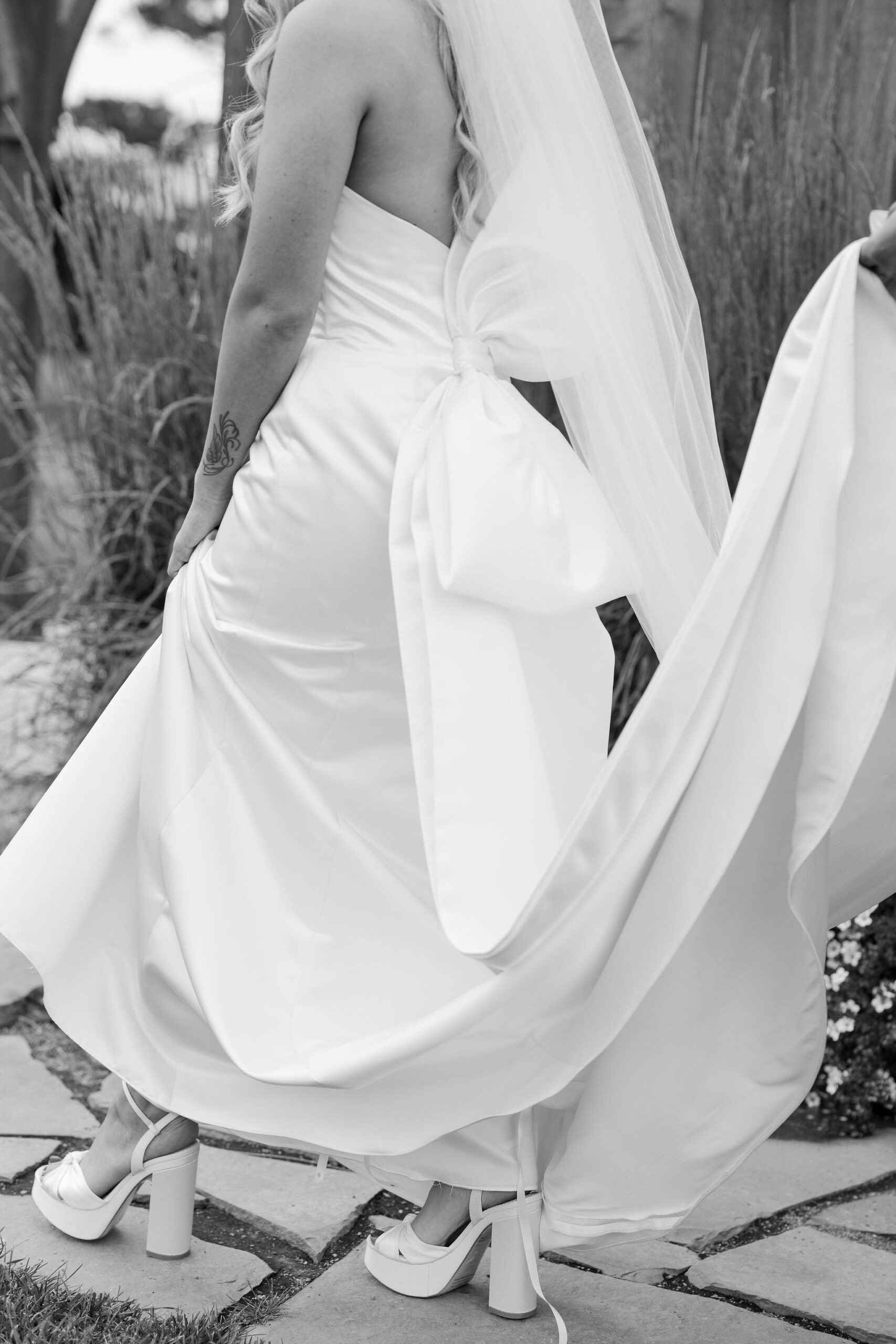 A close-up, black and white shot of the bride's dress detail as she walks through the grass at Copper Rose Ranch Wedding Venue. The elegance of the gown is highlighted by the natural setting, captured by Haley J Photo, a Montana Wedding Photographer.