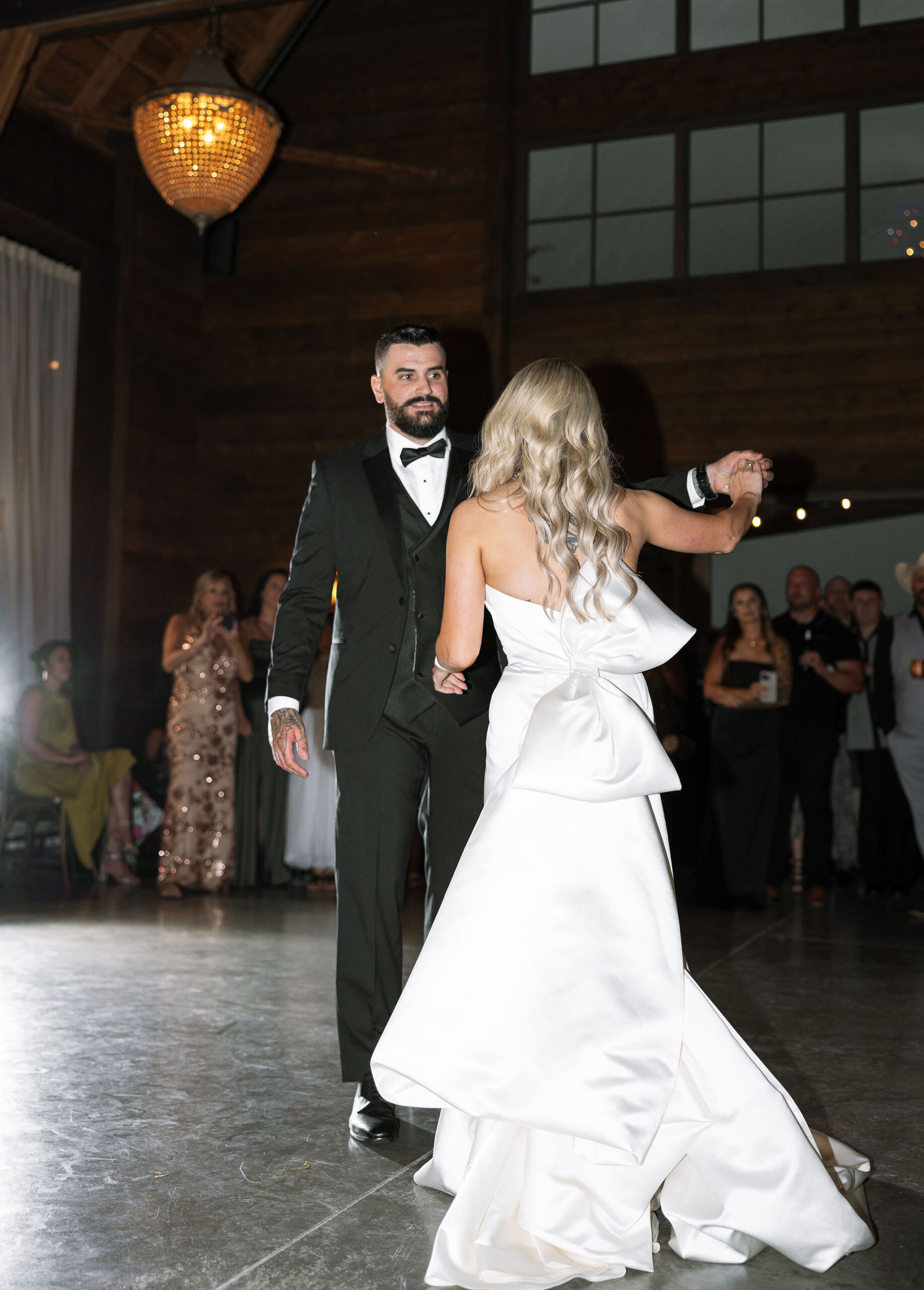 The bride and groom dance in the rustic barn at Copper Rose Ranch, with the groom leading the bride across the floor. The image, taken by Haley J Photo, a Montana Wedding Photographer, captures the joy and elegance of the moment.