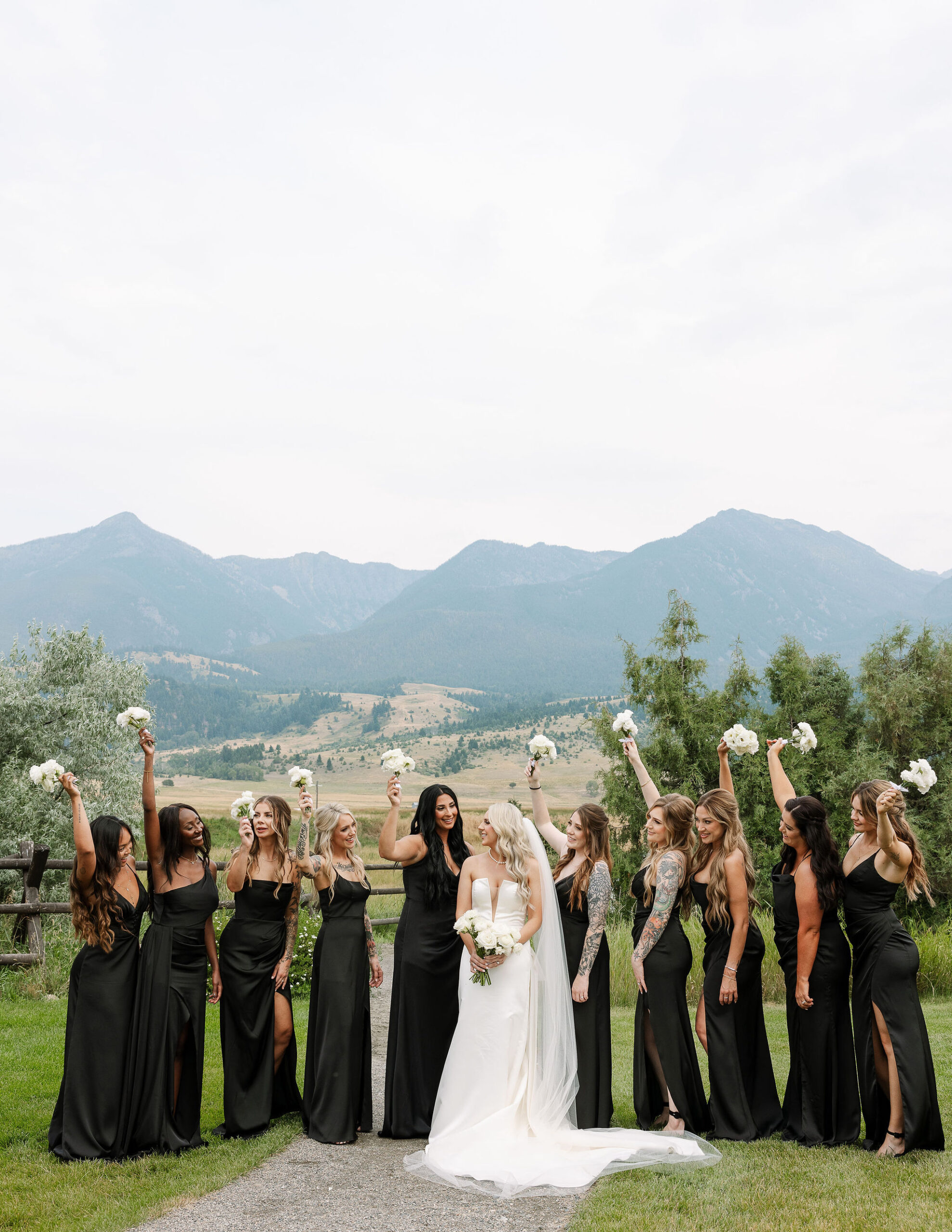 The bride, dressed in a strapless white gown, stands with her bridal party at Copper Rose Ranch Wedding Venue in Montana. The group is framed by the picturesque mountain backdrop, beautifully photographed by Haley J Photo.

