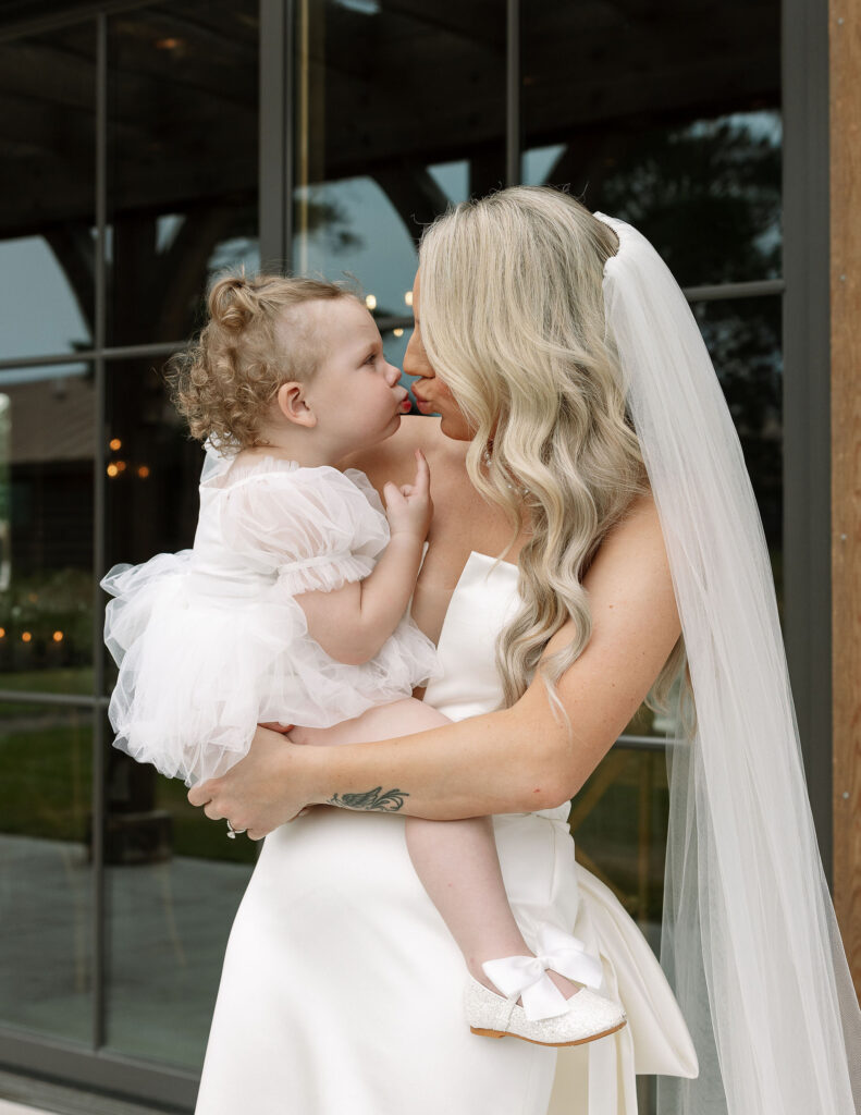 The bride holding a young girl, both smiling warmly at each other, outside Copper Rose Ranch Wedding Venue. Captured by Haley J Photo, a Montana Wedding Venue Photographer.