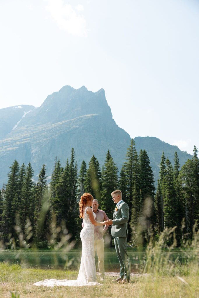 Jessica and Tanner standing by the serene waters of Lake Josephine, surrounded by lush greenery during their Glacier National Park elopement.