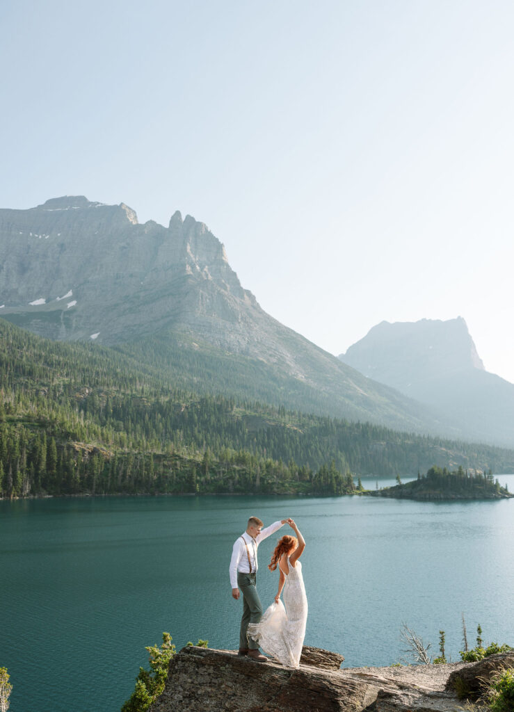 Bride and groom standing by a lake with a stunning mountain backdrop during their Glacier National Park elopement.