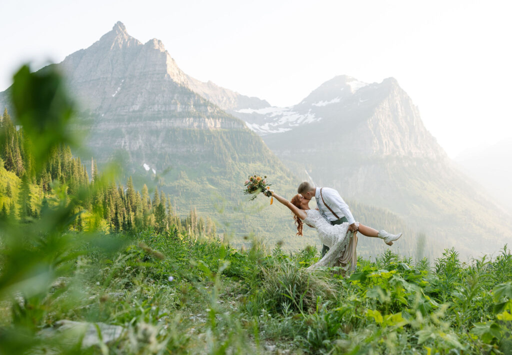 Groom lifting the bride in a joyful dip, with mountains in the background, during their Glacier National Park elopement.