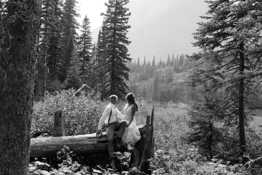 Bride and groom sitting on a log, enjoying a quiet moment in the forest during their Glacier National Park elopement.