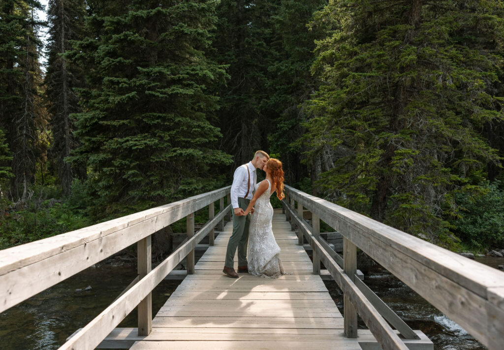 Bride and groom sharing a kiss on a wooden bridge surrounded by lush forest during their Glacier National Park elopement.