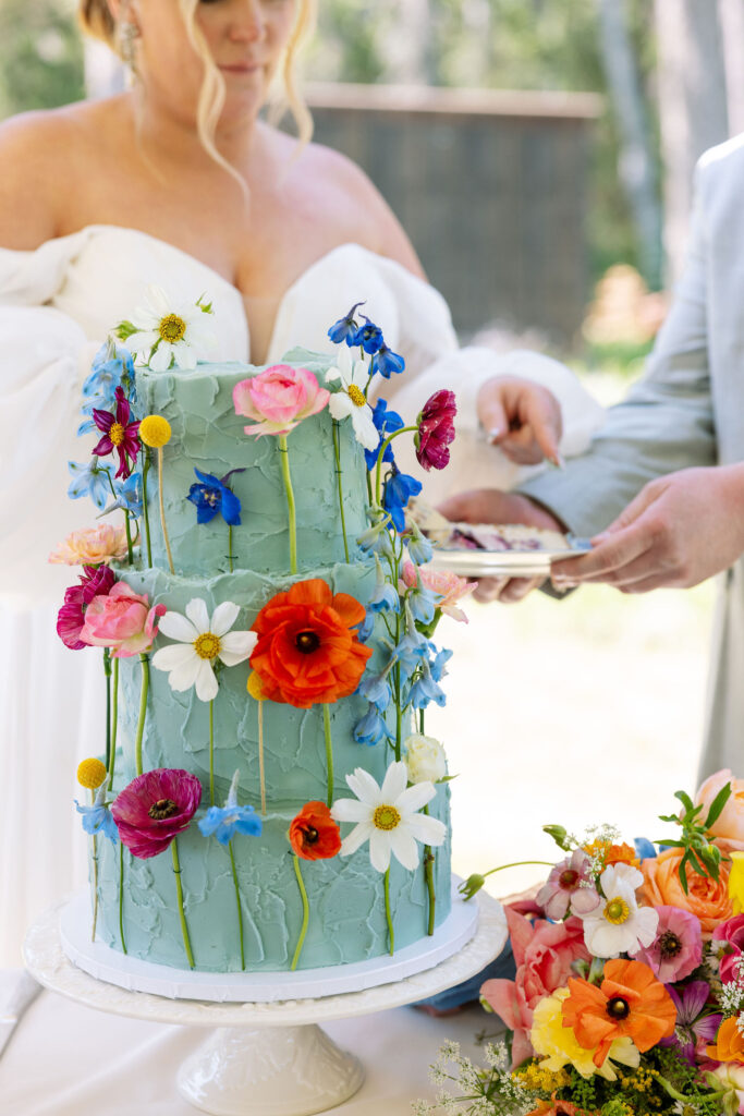 Bride and groom cutting their colorful wedding cake decorated with fresh flowers