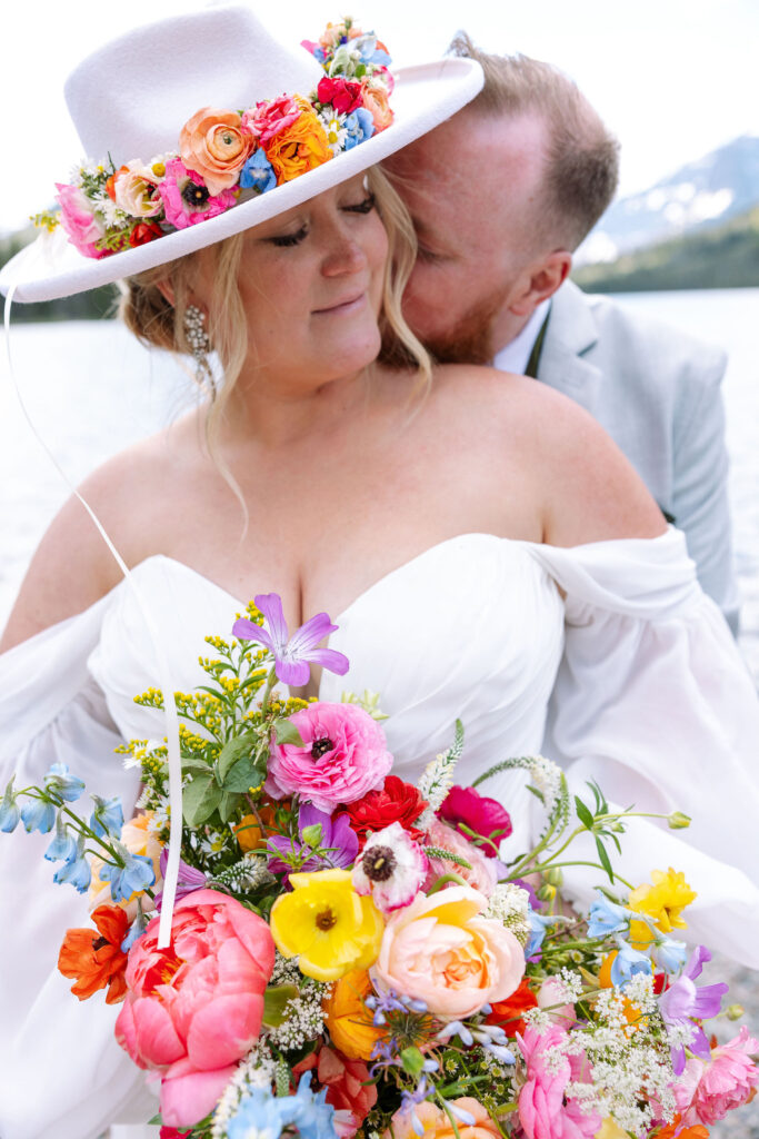 Bride and groom walking through a meadow with mountains in the background and her flowing veil catching the breeze