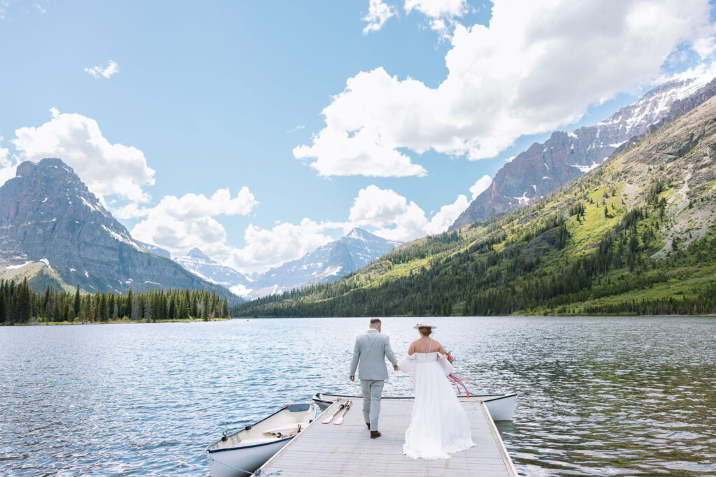 Bride and groom embracing in front of a scenic lake and mountain backdrop in Glacier National Park