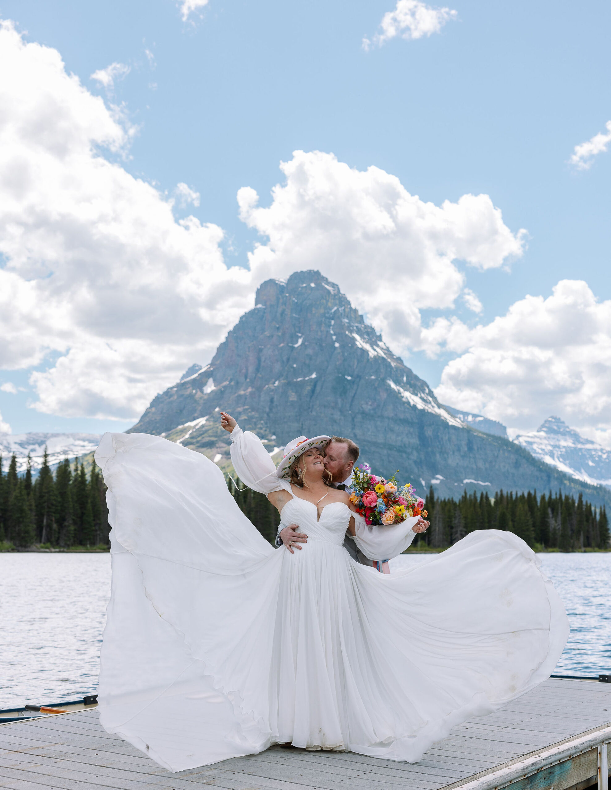 Bride holding a colorful bouquet of flowers, standing by a cabin with a mountain in the background